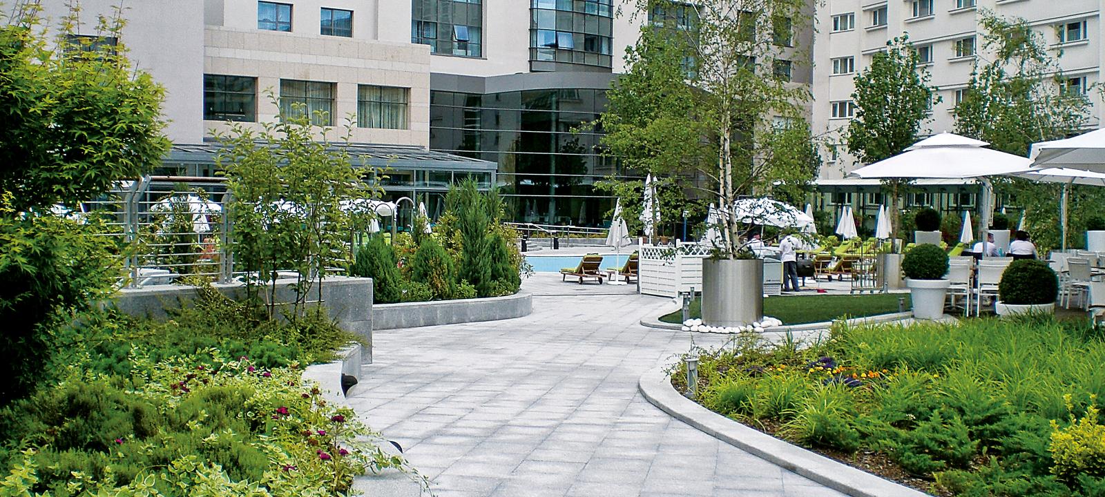 Curved walkways, plant beds and swimming pool surrounded by parasols and sun beds